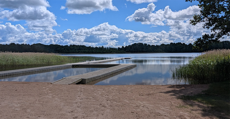 En sjö med en lång brygga. I förgrunden en sandstrand.