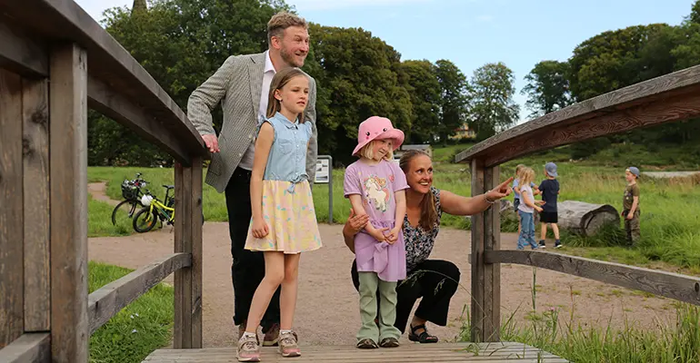 Två vuxna och två barn på en bro. Kvinnan hukar sig ned och pekar på något utanför bild.