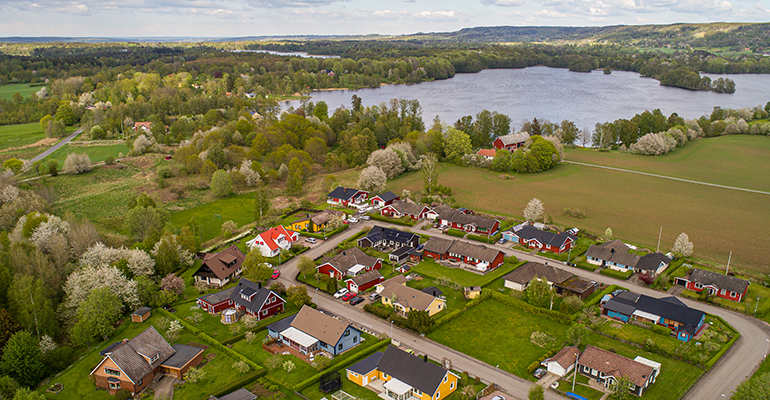 Flygfoto över ett litet samhälle med några hus. Flera träd och en större sjö längre bak i bild.