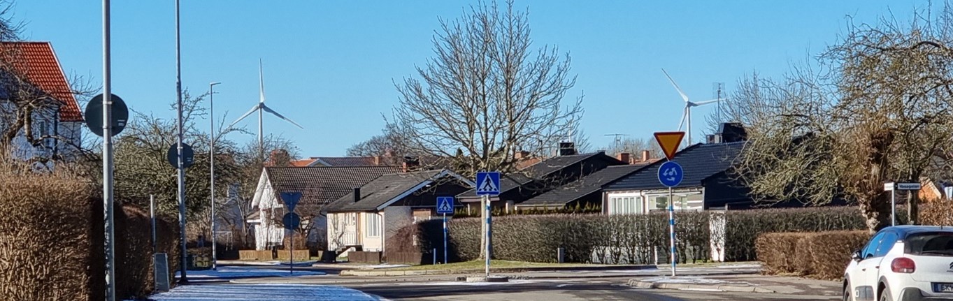 Foto med hus i förgrunden och vindkraftverk i bakgrunden