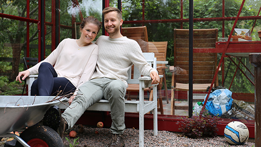 Hanna och Olle sitter på en bänk framför ett växthus i deras trädgård. 