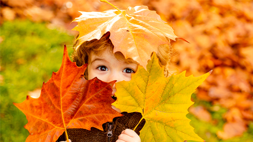 litet barn som håller färgglada löv framför ansiktet